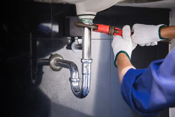 Plumber fixing white sink pipe with adjustable wrench.