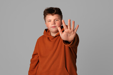 Serious-looking teenager boy keeps palm raised makes restriction or denial gesture, prohibit...