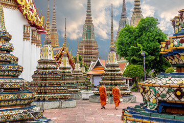 Two monks walking alongside stupas at the Wat Pho Temple in Bangkok - obrazy, fototapety, plakaty