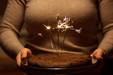 Woman holding a plate with brownie pie decorated with burning sparklers