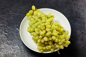 Branch of ripe grape on plate. Juicy grapes on wooden background, closeup. Grapes on dark kitchen table with copy space
