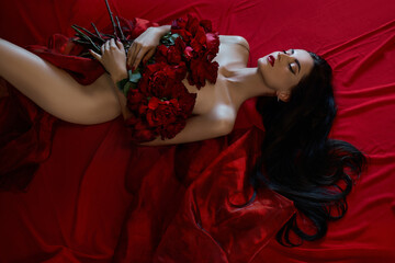 Beautiful sexy brunette with a bouquet of red roses lying on the floor, naked body parts, erotic...