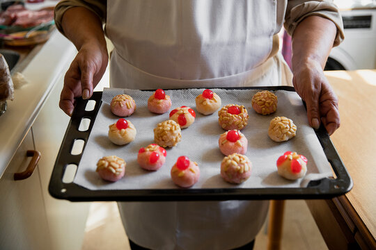 Woman with apron holding panellets in baking sheet at kitchen