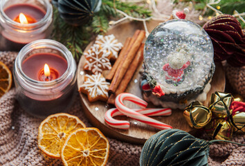 A snow globe and christmas candles with branches of fir.
