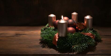 First Advent wreath with copper colored candles and Christmas decoration baubles on a rustic wooden...
