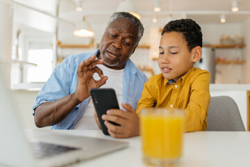 Mixed race grandson showing his grandfather how to use a new phone. He is old so the kid must explain how apps are working. - 469253367
