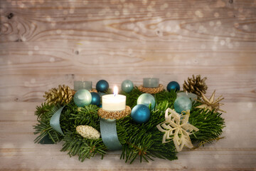 Advent wreath series number one with a lit candle, blue Christmas baubles and decoration on a...
