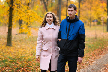 A couple walks in an autumn park along a path. Beautiful nature and trees with yellow leaves.