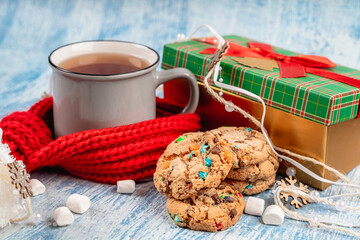 A cozy mug of hot tea drink and cookies stands with a red knitted scarf and a gift box during the New Year holidays during the winter holidays