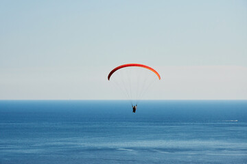 Fototapeta na wymiar Paragliders soar high in the sky over the deep blue sea. Extreme sport and leisure activity on vacation