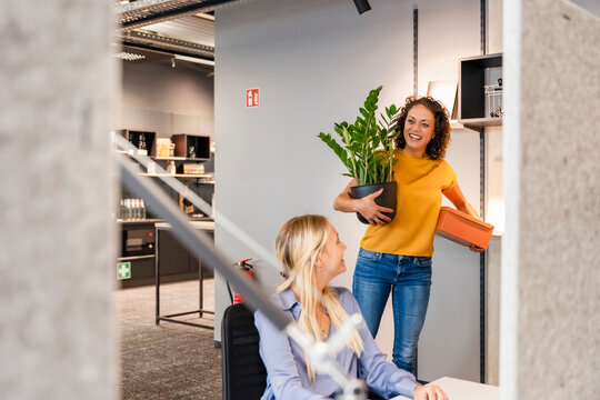 Smiling businesswoman with potted plant and box relocating in office