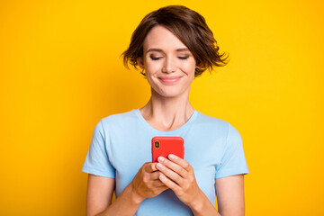Photo of young attractive girl happy smile look use cellphone chat type browse isolated over yellow color background