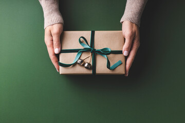 Female hands holding Christmas gift box tied velvet ribbon on Green background.