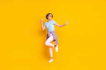 Fototapeta na wymiar Full length photo portrait of woman showing two v-signs standing on one leg dancing with tight waist shirt isolated on vivid yellow colored background