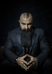 Stylish man with a black beard in a black suit with graceful hands looks serious