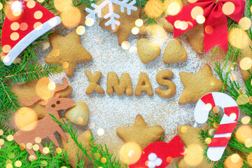 Christmas cookies in the form of XMAS lettering in the form of gingerbread cookies stars on the background of a rolling board with powdered sugar and Christmas decorations and tree around