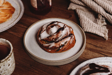 Freshly baked poppy swirl buns (or sweet rolls) glazed icing and chocolate with cocoa mug and jam on wooden table. Cosy winter breakfast. Selective focus