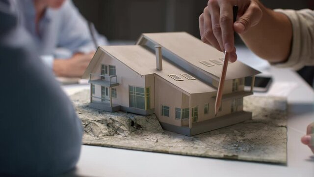 Architects and designers working on house layout in office studio. Group of creative people at desk talks on maquette and discusses home design. Specialists looking at prototype of mini model close-up
