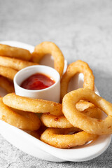 Battered onion rings in a dish,  with a tomato ketchup dip. On a concrete background
