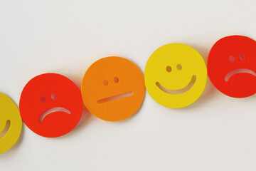 Chain of yellow, orange and red paper faces with positive, neutral and negative expression on white...