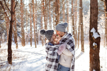 Happy smiling couple hugging under a plaid outdoors in winter forest, valentine's day.