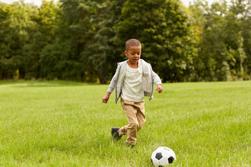 childhood, leisure games and people concept - little boy with ball playing soccer at summer park