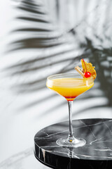 citrus and pineapple cocktail on marble table close up. tropical cocktail with shadow of tropical plants branch on background