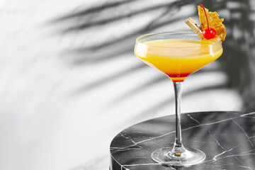 citrus and pineapple cocktail on marble table close up. tropical cocktail with shadow of tropical plants branch on background