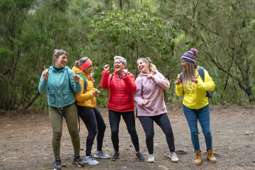 Group of women with different ages and ethnicities having a funny moment dancing during a walk foggy woods - Adventure and travel people concept
