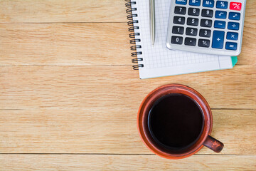 Cup of coffee, notebook with pen and calculator on a wooden table. Copy space