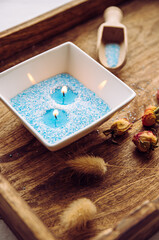 Blue and white granulated wax crystals to create candles by pouring in bowl and inserting wick. Handmade sand candle in white ceramic bowl on wooden tray, spoon with candle wax powder.