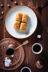 Turkish or Bosnian dessert called Baklava with pistachio served with traditional Turkish or Bosnian coffee set on a wooden board in moody atmosphere