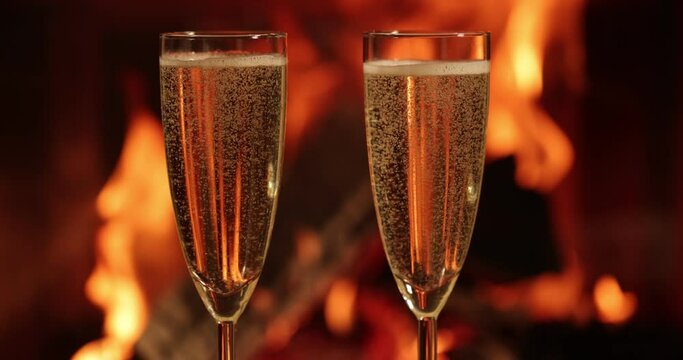 Sparkling champagne wine in glasses in front of the warm fireplace. 4k .