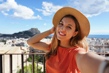 Tourist girl on Castillo de San Fernando taking selfie photo with Alicante cityscape and Mount Benacantil with Castillo de Santa Barbara on the background. Girl takes self portrait in Alicante, Spain.