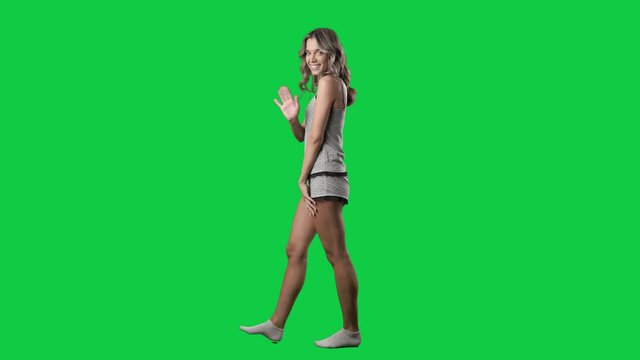 Side view of walking woman in pajama turning and waving happy at camera. Full body isolated on green screen background