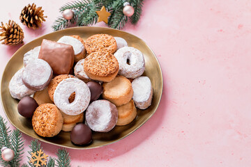 Fototapeta na wymiar Holiday delicacies polvorones and mantecados in golden plate on pink table overhead