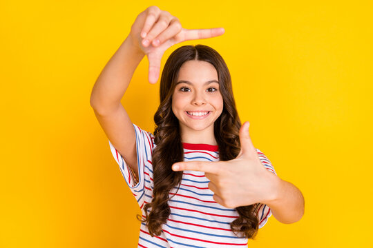 Photo of young beautiful positive smiling girl taking picture with fingers wear striped t-shirt isolated on yellow color background