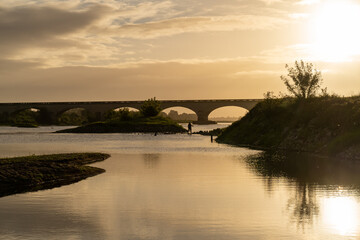 Fototapeta premium A soft golden sunset illuminates a bridge over the Loire River, casting long shadows and peaceful reflections