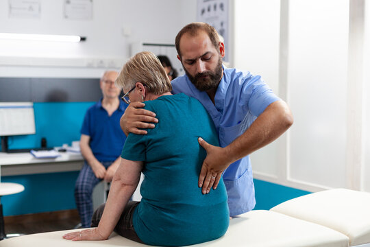 Medical assistant treating woman with back and spine pain for physical recovery. Chiropractic nurse giving assistance to retired patient with spinal cord injury and orthopedic care
