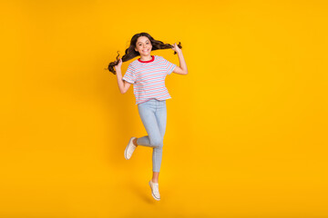 Full length photo of young girl happy positive smile have fun jump up hands touch hair isolated over yellow color background