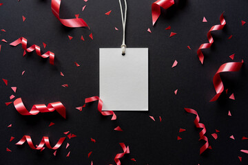 close u top view on blank white tag paper with rolling ribbon and confetti on black background with copy space for merry christmas, happy new year festival and black friday sale season concept