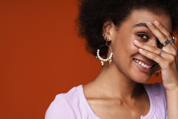 Young black woman wearing earrings smiling and covering her face
