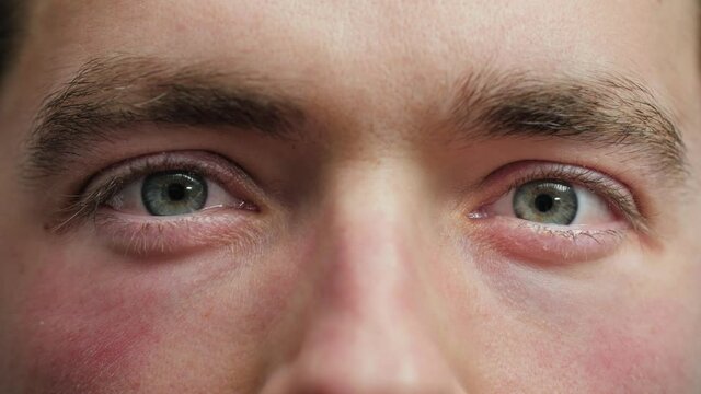 Close up of Man's face. Attractive boy opening his beautiful blue eyes. Caucasian young male model with blue, green, grey eyes looking at camera. Slow-motion, macro extreme close-up, 4K.
