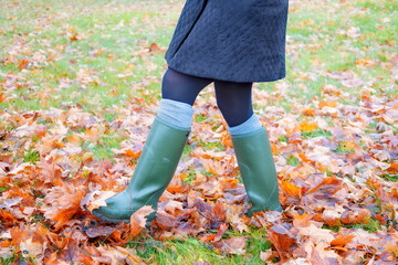 Woman in rain boots kicking autumn leaves