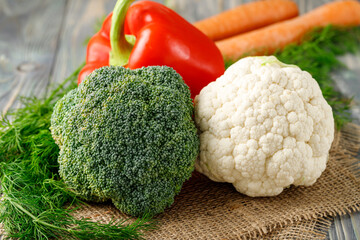 Fresh  raw cauliflower, broccoli, red bell pepper, carrots and dill herb on rustic wooden table. Vegetables closeup on  vintage jute