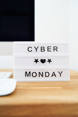 Cyber monday is written on a light box. The light box is on a wooden desk.Cyber week information. Computer in the background is blurred. Cyber monday sale concept. 