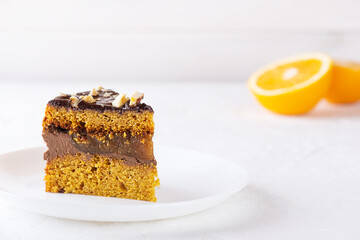 Piece of vegan pumpkin pie with chocolate, oranges and nuts on a white plate. Sugar, gluten and lactose free.