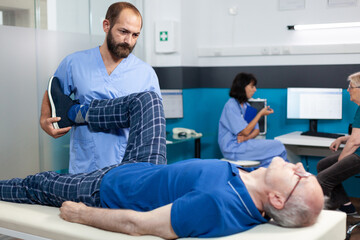 Fototapeta premium Orthopedic specialist assisting old patient with leg joint injury for physiotherapy. Chiropractor doing physical exercise to relieve pressure on muscle for recovery and healthcare