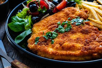 Breaded fried pork chop with French fries and fresh vegetables on wooden table
