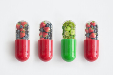 Unique green vitamin pill supplement amongst red fruit pills, food colours concept